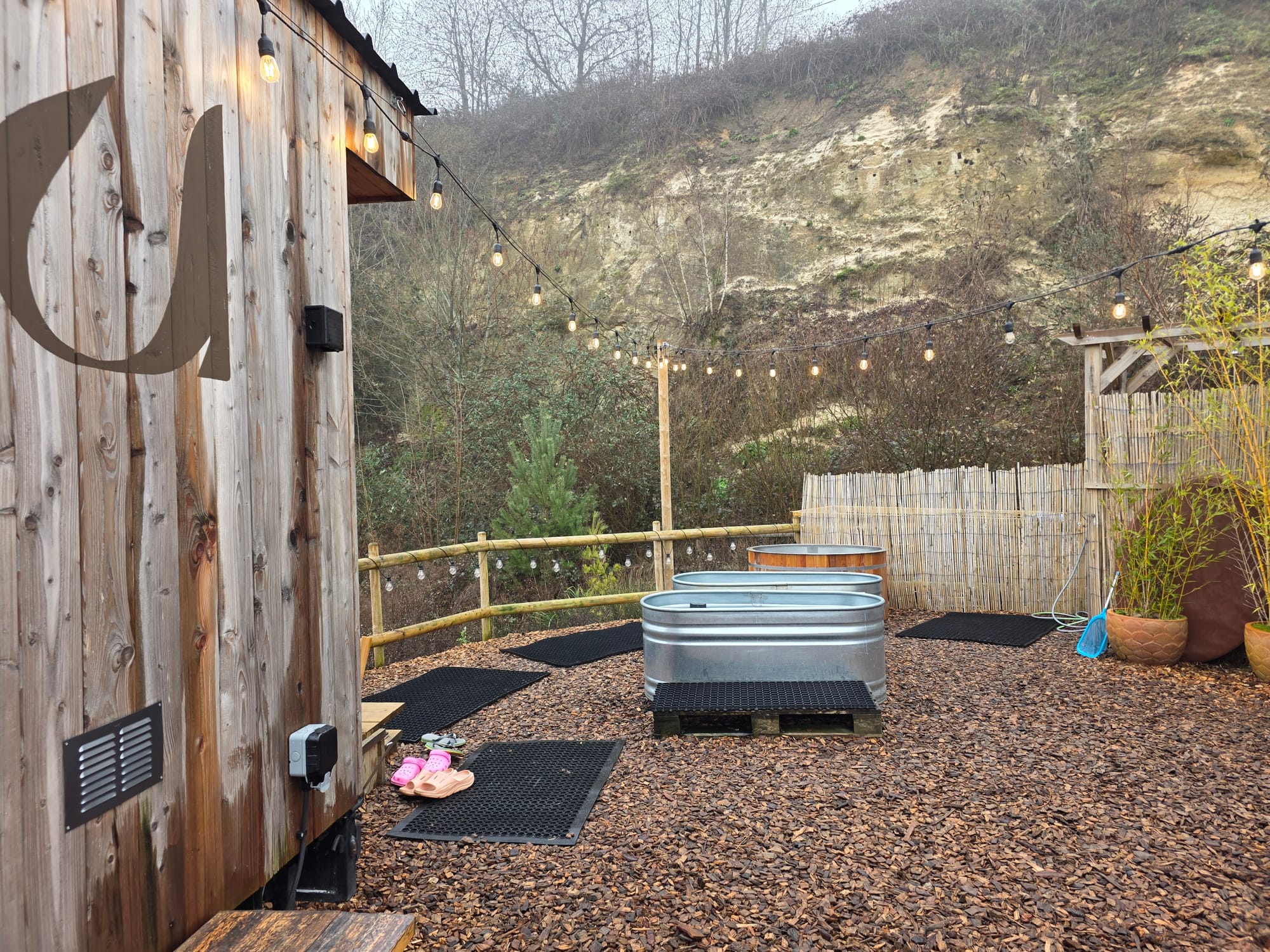 Plunge area next to Savu sauna showing bark ground and rubber mats leading to the cold tubs.