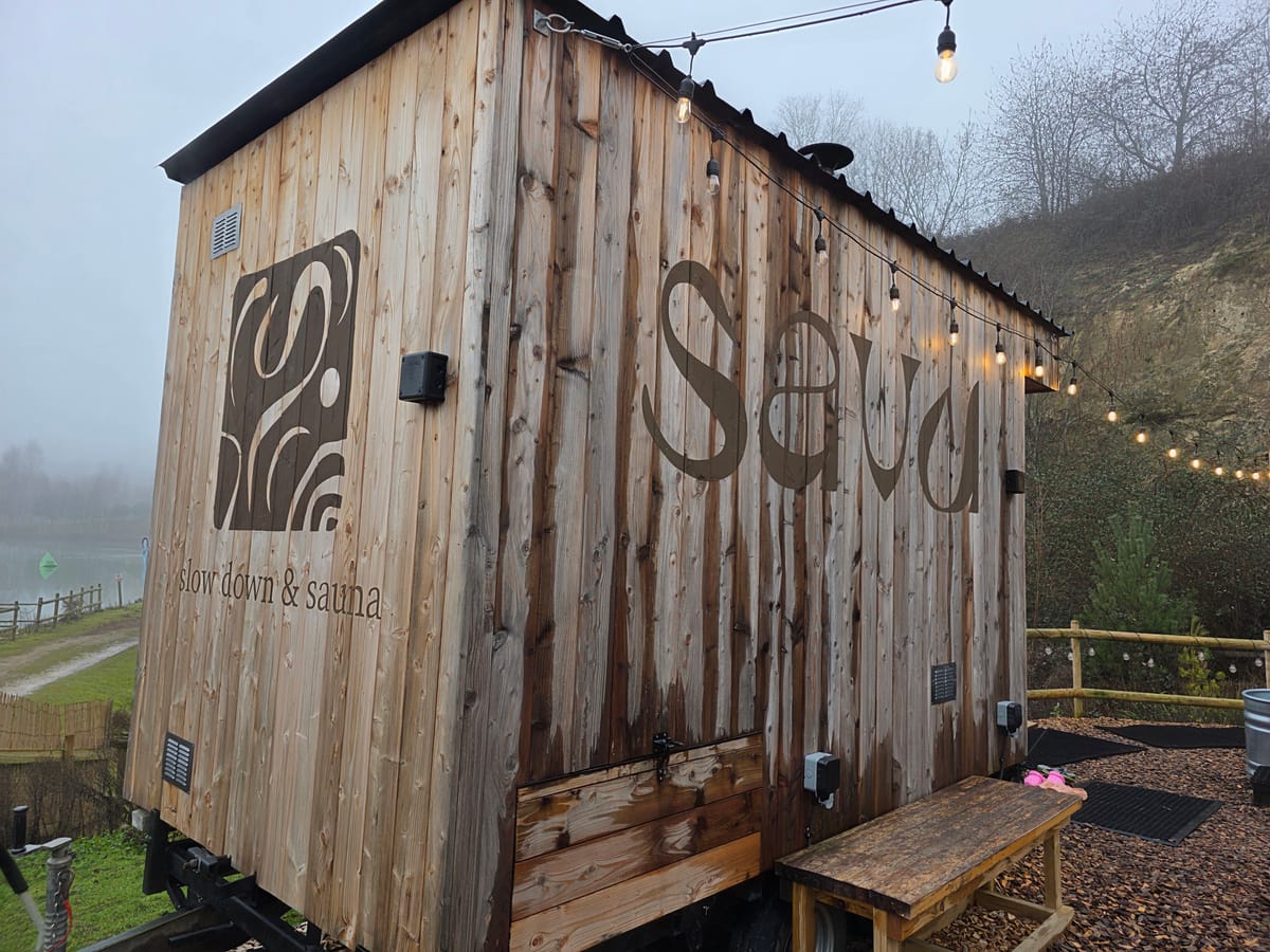 Exterior of Savu sauna cabin at Buckland Park Lake in Surrey with string lights and plunge area nearby.